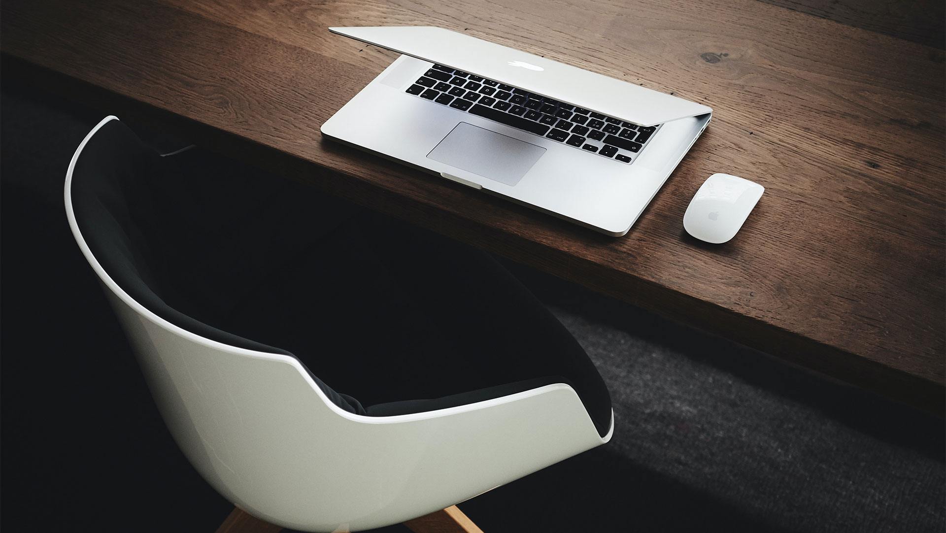 laptop slightly closed on a wooden desk with a mouse next to it