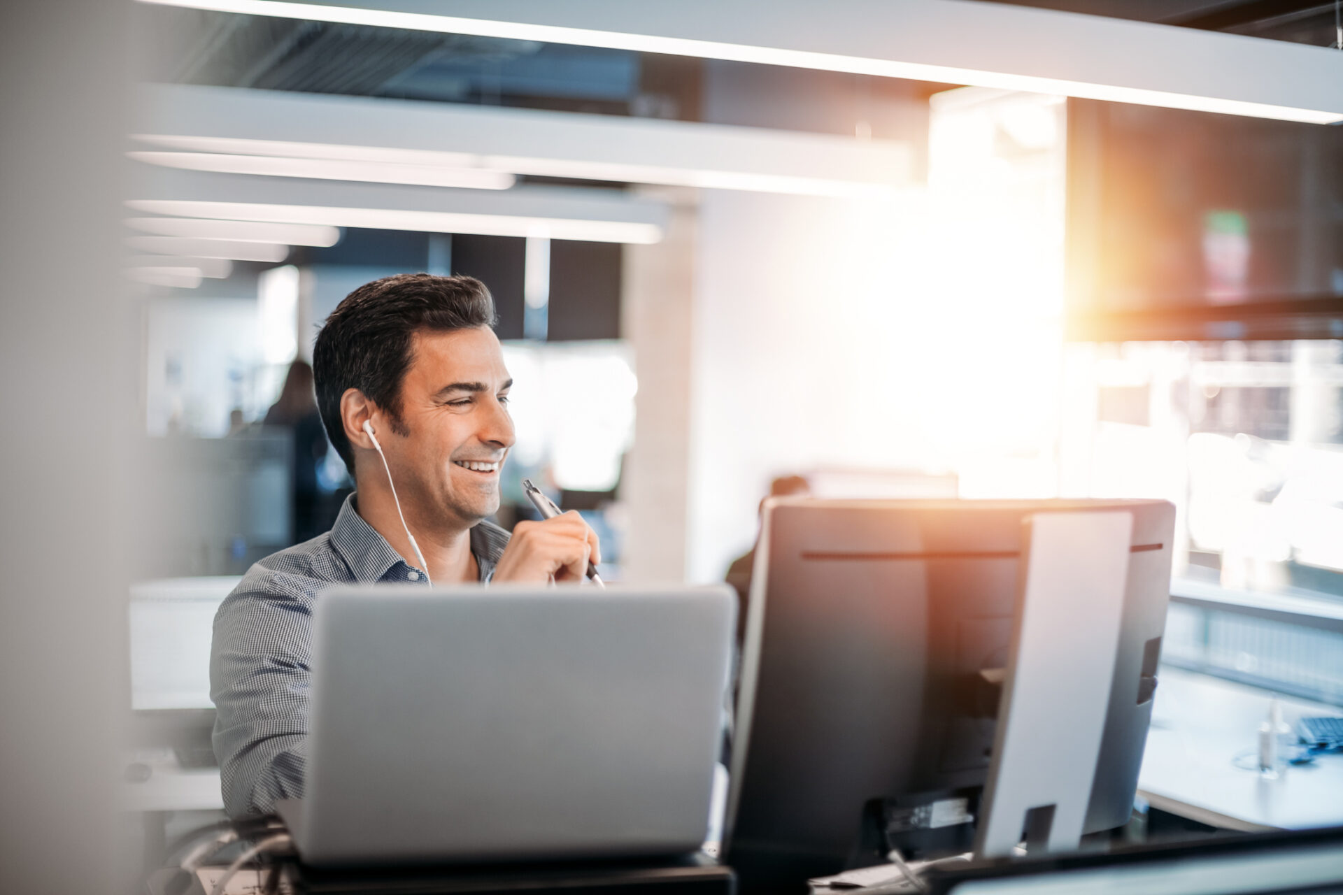 man smiling while working behind a desk with two computer screens