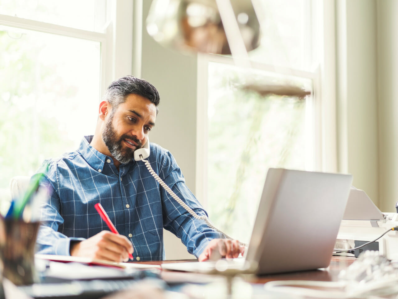 A man working on a laptop while talking on the phone.