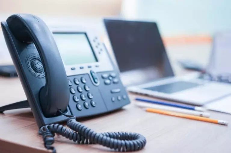 A laptop is sitting on a desk next to a VOIP enabled telephone.